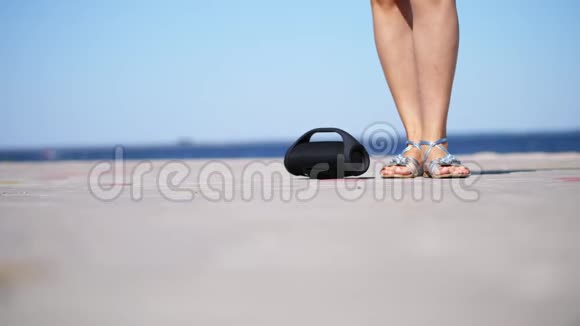 特写迷你音乐蓝牙便携式黑筒无线扬声器穿着银色凉鞋的女性腿视频的预览图