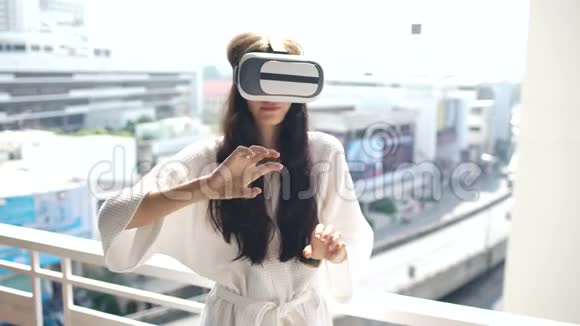 女士穿着浴袍戴着虚拟现实耳机站在酒店客房阳台上有VR体验视频的预览图