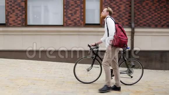 4k视频时尚时髦的红胡子男人骑着老式黑色自行车走在老街上视频的预览图