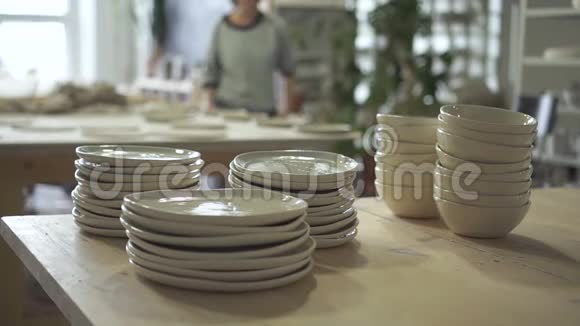 在明亮的陶瓷工作室里一堆一堆的盘子和碗立在木桌上视频的预览图