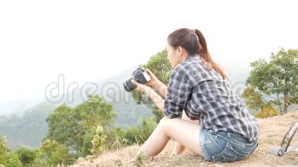 年轻活跃的亚洲旅游女性旅游摄影师带着背包在山上用数码相机拍照视频的预览图