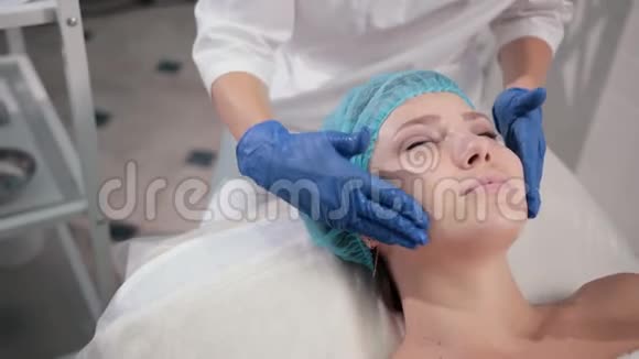 带蓝色手套的护士医生用轻动作做女性面部按摩视频的预览图