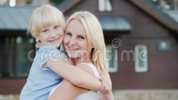 一位母亲和一个小女儿拥抱在他们新家的背景下看着镜头的画像视频的预览图