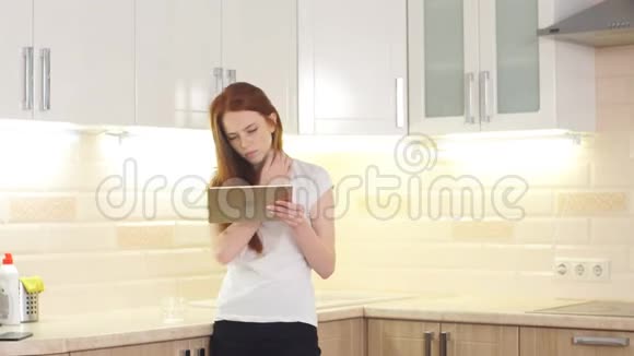 开朗的红发女孩在家里厨房用平板电脑视频的预览图