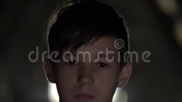 一个严肃悲伤的男孩在黑暗的房间里看着摄像机脸上疼痛视频的预览图