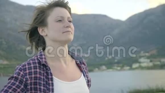 年轻女子站在岛上的悬崖上看着海洋日落视频的预览图