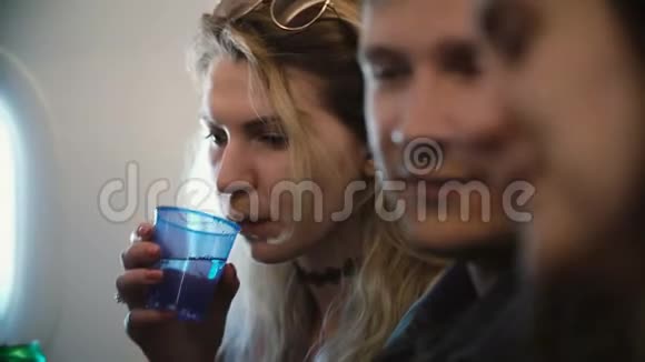 一群年轻人坐在飞机上靠近窗户和饮用水朋友要乘飞机旅行视频的预览图