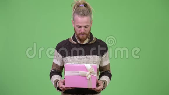 快乐英俊的大胡子男人微笑着一边拿着礼品盒思考着视频的预览图