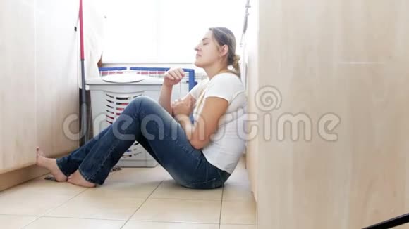 4K画面显示年轻女性坐在地板上洗衣服靠在洗衣机上视频的预览图