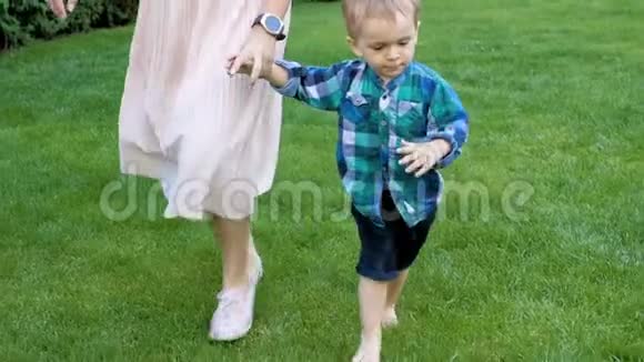 在公园里可爱的赤脚幼儿男孩牵着妈妈的手在草地上散步视频的预览图