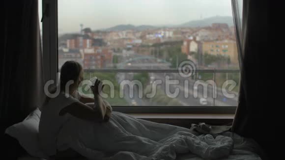女人躺在床上喝茶看着城市视频的预览图