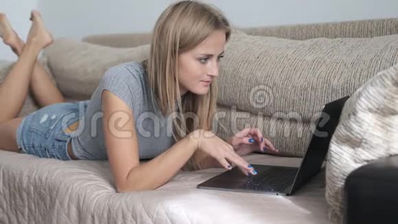 在家里用笔记本电脑工作的女人躺在沙发上打字的女人视频的预览图