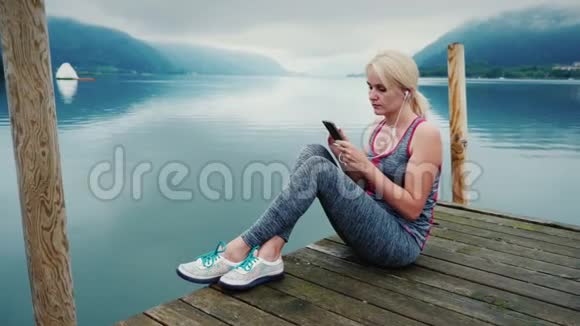 一个女人坐在木墩上看着奥地利的山和山湖使用智能手机视频的预览图