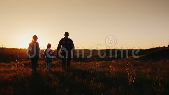 stadicam慢动作镜头一个由三个人组成的年轻家庭将要经受日出或日落后侧剪影视频的预览图