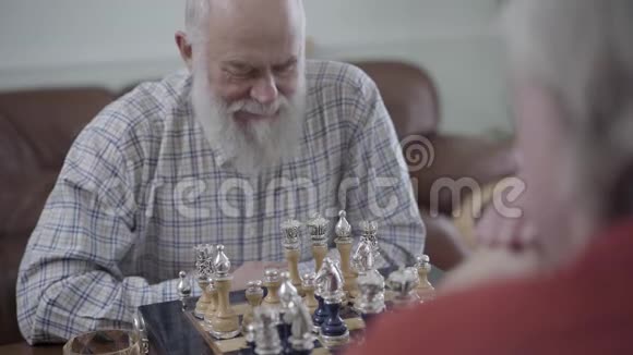 两个老人下棋坐在家里的皮革沙发上蓄胡子的人在想哪个棋子能动视频的预览图