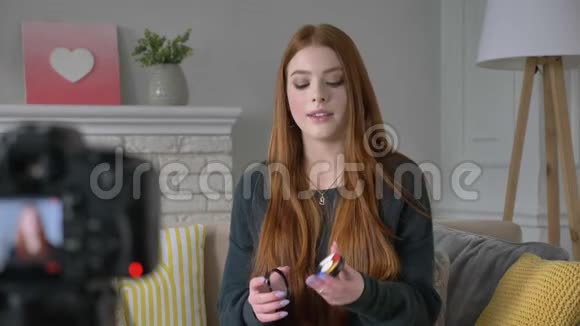 年轻的红发女孩博客作者微笑着对着镜头说话展示了一个新的购买化妆品眼影托盘家视频的预览图