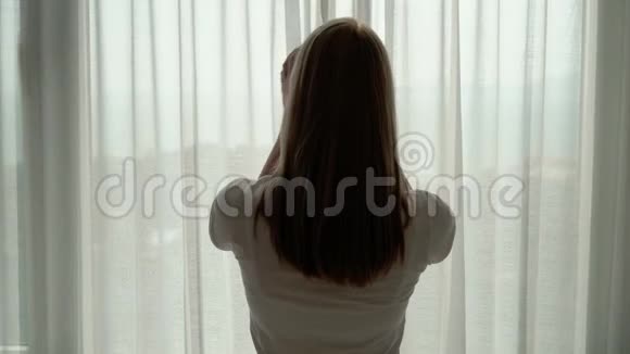 穿白色t恤的女人揭开窗帘看着窗外在外面欣赏海景视频的预览图