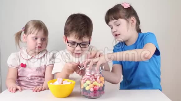 三个快乐的孩子从罐子里拿出棉花糖在桌子上吃视频的预览图