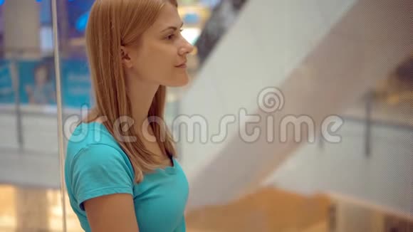 幸福微笑的年轻女子穿着绿松石T恤坐在购物中心的电梯里仰望视频的预览图