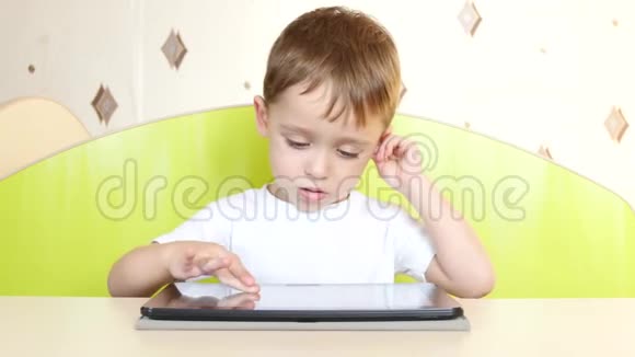 坐在桌子旁的小男孩触摸平板电脑的电子显示器一个孩子在玩手提电脑视频的预览图