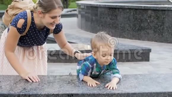 慢动作视频可爱的微笑幼儿男孩看喷泉与母亲视频的预览图