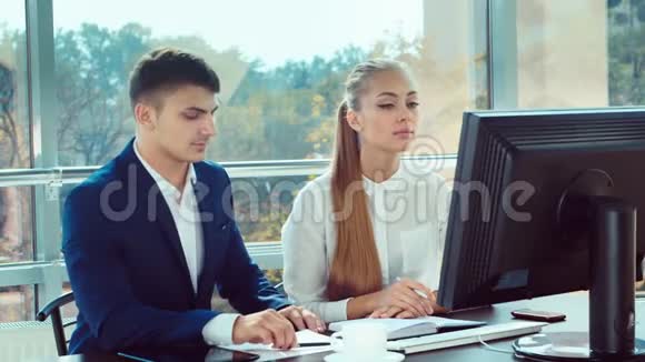 两个年轻人在办公室工作他们一起看电脑显示器视频的预览图