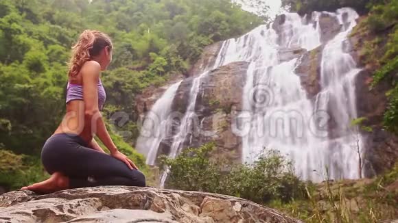 侧视图金发女孩坐在瀑布前的瑜伽姿势视频的预览图