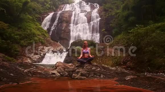 女孩在瀑布小湖后面的瑜伽位置放松视频的预览图