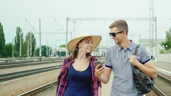 快乐的年轻夫妇带着智能手机去火车站概念订购网上门票视频的预览图