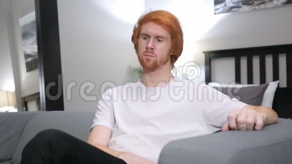 可怜的红头发男人在想坐在卧室的沙发上视频的预览图