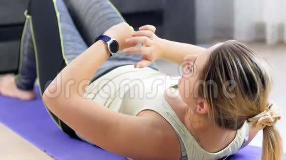 4k视频年轻女子躺在健身垫上用智能手表测量腹部前的身体参数视频的预览图