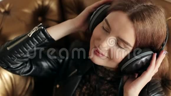 一个穿着皮夹克戴着立体声耳机听音乐的年轻女孩视频的预览图