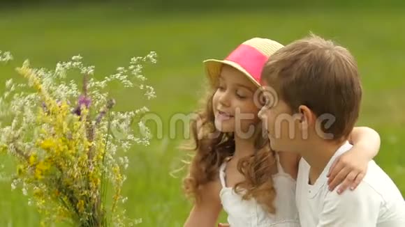 孩子们坐在公园的草坪上嗅着刚收获的田野花慢动作视频的预览图