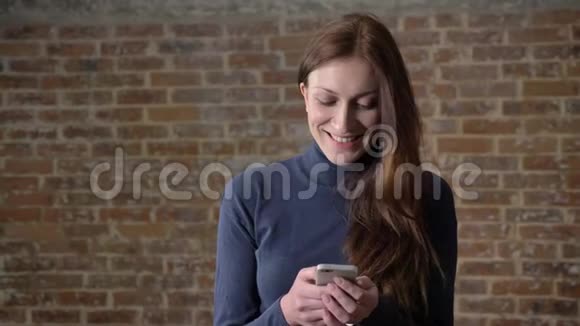 棕色头发的女孩正在智能手机上输入信息微笑交流理念砖背景视频的预览图