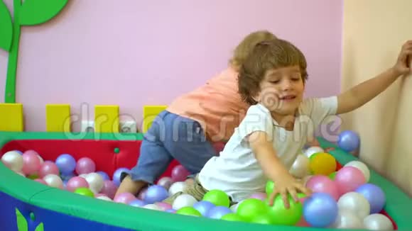 快乐的男孩和女孩在多种颜色的球池里玩托儿所视频的预览图