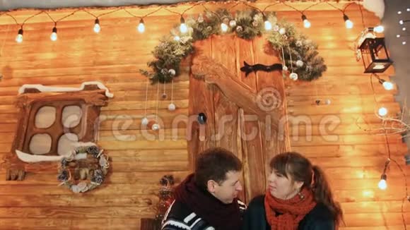 一对相爱的夫妇坐在木制童话房子的门廊上互相享受圣诞节和新年主题视频的预览图