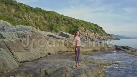 女孩站在瑜伽姿势在石头上波浪冲浪视频的预览图