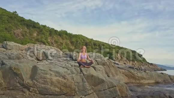 金发女孩在大型高岩石上放松瑜伽姿势视频的预览图