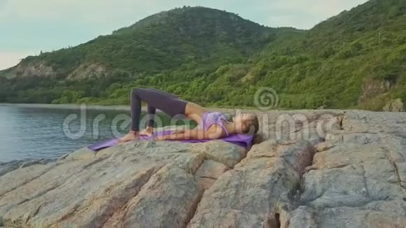 Flycam绕着女孩在岩石海岸的垫子上做瑜伽视频的预览图