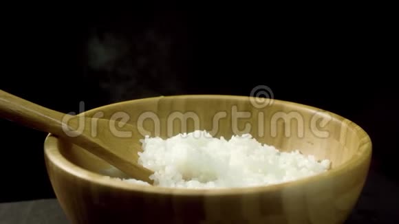 用木搅拌勺将蒸饭装在木碗里在黑色背景上隔离新鲜煮熟的米饭视频的预览图