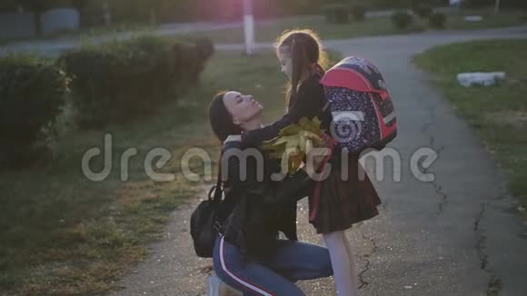 一个女人从学校遇到她的小女儿穿着校服的女孩背着背包拥抱并亲吻她的妈妈慢慢视频的预览图