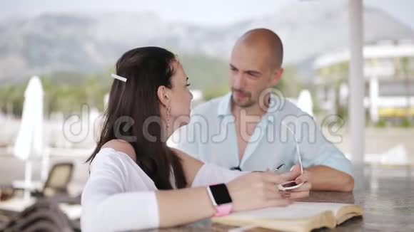 年轻夫妇在码头的酒吧调情年轻夫妇在你的电话里看照片在酒吧聊天视频的预览图