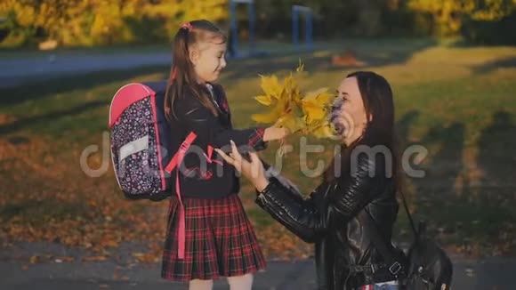 一位快乐的母亲从学校遇到了她的小女儿妈妈用花束拥抱和亲吻穿着校服的女儿视频的预览图