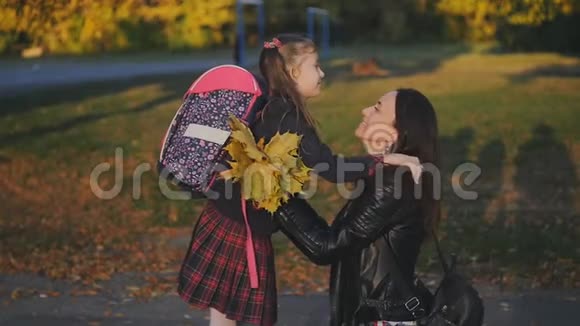 女人从学校遇到她的小女儿穿着校服的女孩背着背包拥抱并亲吻她的妈妈慢慢视频的预览图