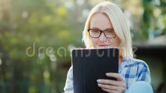 一位年轻女子在她家的院子里享受一块石碑的肖像概念技术和远程学习视频的预览图