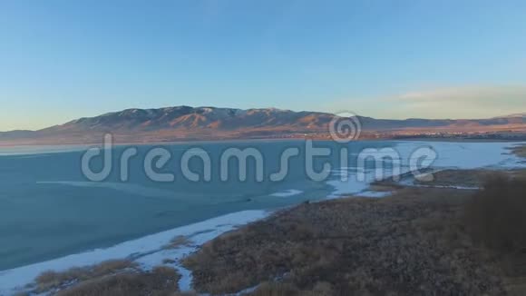一个冰冻的湖泊的空中全景然后沿着海岸线在雾霭之外有雪山视频的预览图