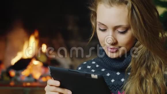 一个有魅力的女人的肖像与平板电脑一起工作背景是点燃的壁炉概念舒适和视频的预览图