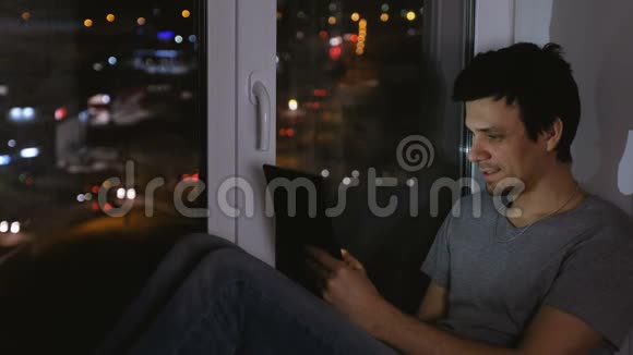 在漆黑的夜晚人们坐在窗台上在平板电脑上浏览网页视频的预览图