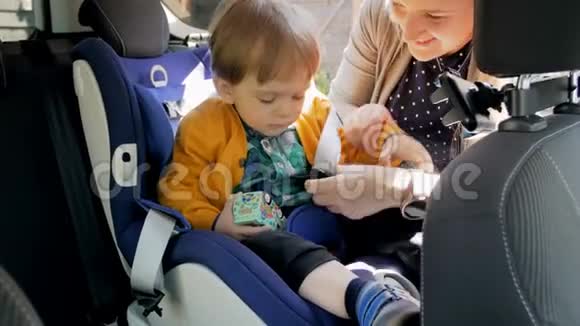 4k视频年轻的微笑母亲调整安全带在她的孩子的安全车安全视频的预览图