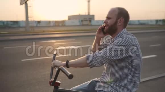 带着bmx自行车的年轻人在街上日落时使用他的手机慢动作视频的预览图